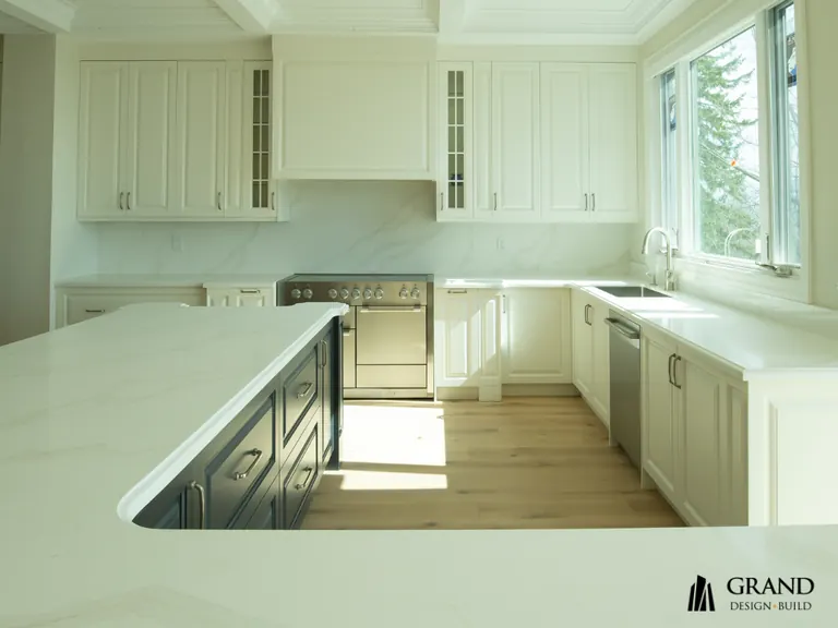 A finished kitchen with a coffered ceiling, cream cabinetry and a dark panelled island