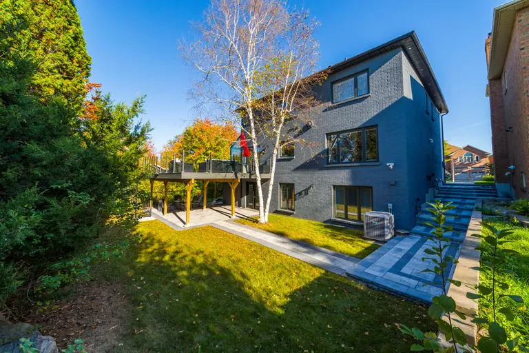 A completed rear addition on a Don Mills home by Grand Design Build: painted brick, full-height windows and an elevated deck over a paved terrace