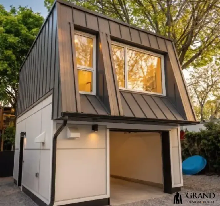 Finished two-storey laneway suite over a garage, in standing-seam metal and white panel, lit from inside at dusk